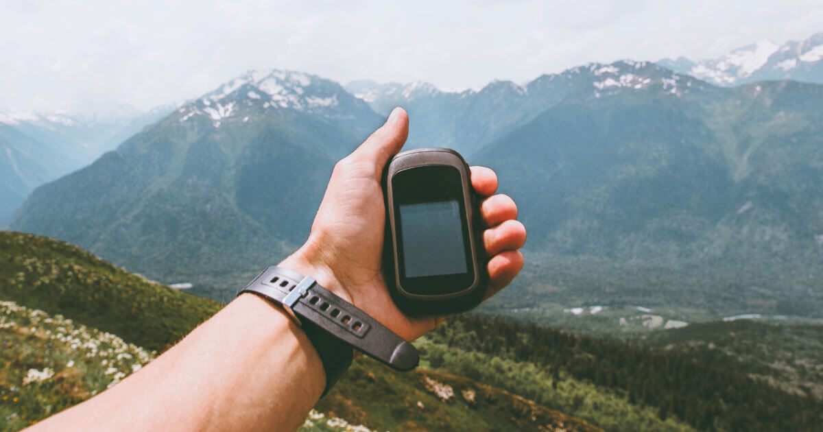 A hiker holding a GPS unit while navigating a mountain region; Unictron's Castle Patch Antenna is uniquely suited for GPS and other positioning devices; find out more at Sourcengine. 