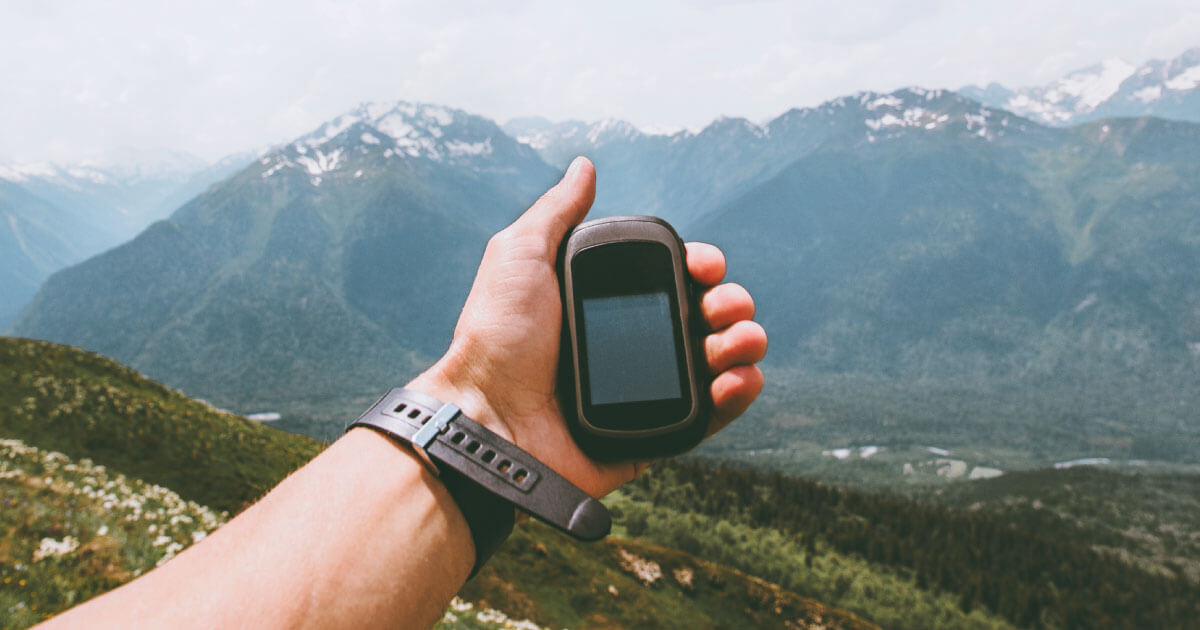 A hiker holding a GPS unit while navigating a mountain region; Unictron's Castle Patch Antenna is uniquely suited for GPS and other positioning devices; find out more at Sourcengine.