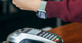 Person paying at a POS machine with a smart watch; for the latest on wearables component trends in 2021, see Sourcengine.