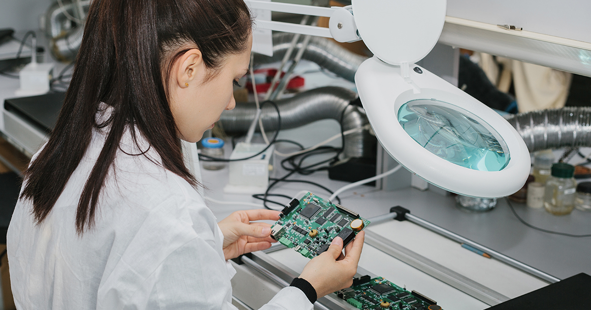 A worker inspecting a fully assembled PCB for flaws and signs of forgery within a laboratory setting.| Sourcengine