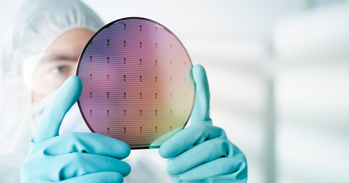 A worker in a clean room suit inspecting a test map for a silicon wafer at eye level | Sourcengine