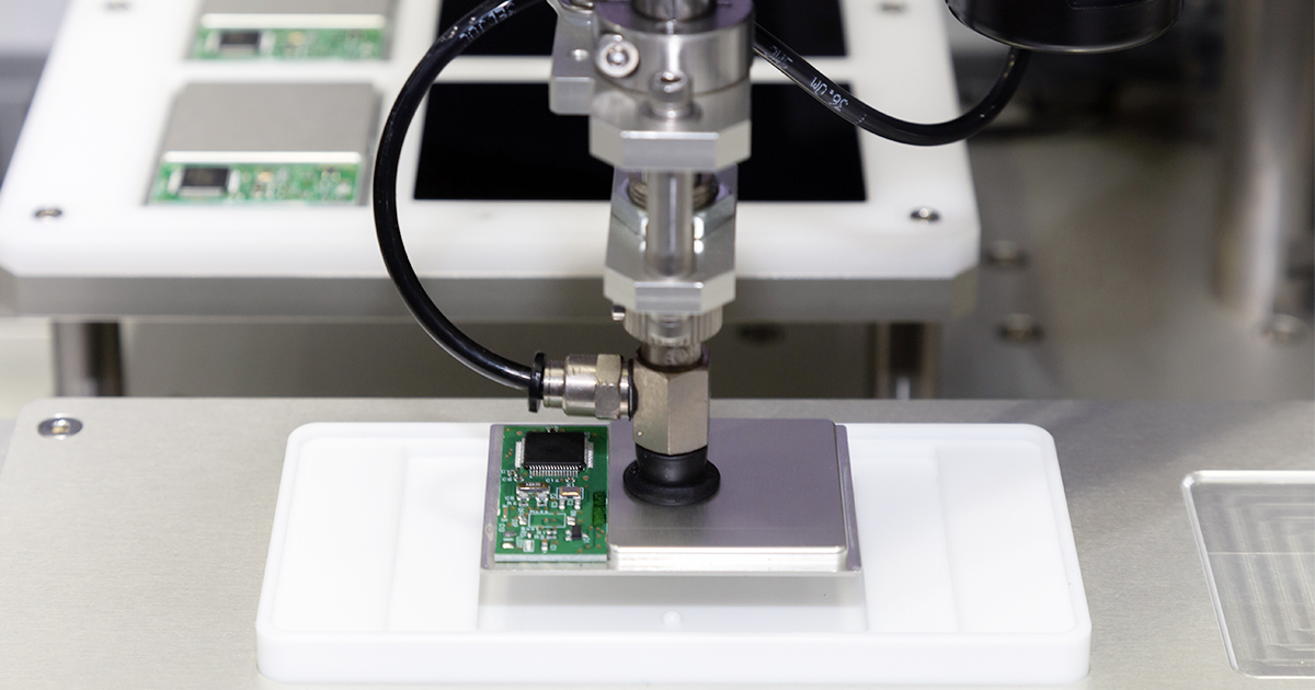 A robotic arm with a vacuum sucker assembles a smartphone with the handset CPU and PCB visible. | Sourcengine