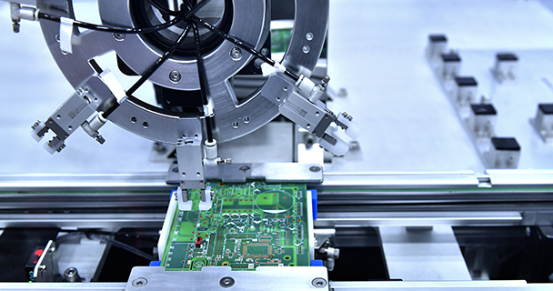 An autonomous robotic arm in the process of assembling a printed circuit board. 