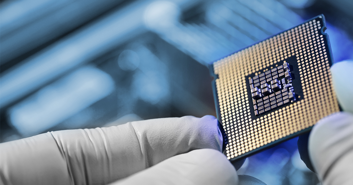 A glove-wearing engineer holding a microprocessor over a computing station. 