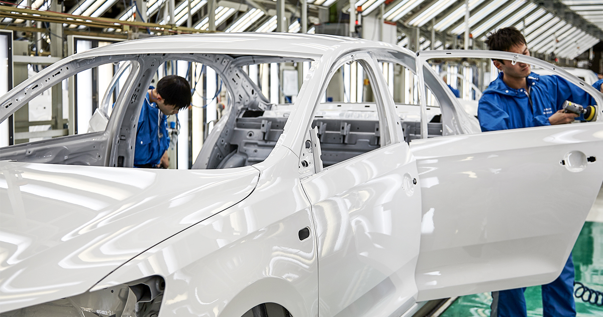 Two autoworkers attend to a sedan chassis inside a modern car factory.