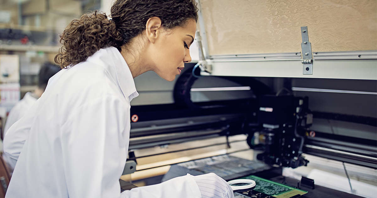 An engineer examines a fully assembled PCB with a handheld magnifying glass.