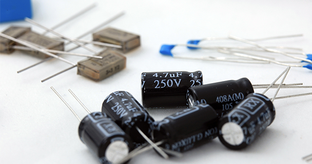 Four piles of electronic capacitors of various sizes and types. | Sourcengine 