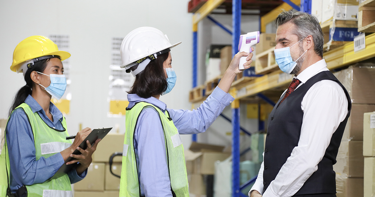 Two workers perform a contactless temperature check on a third staffer.