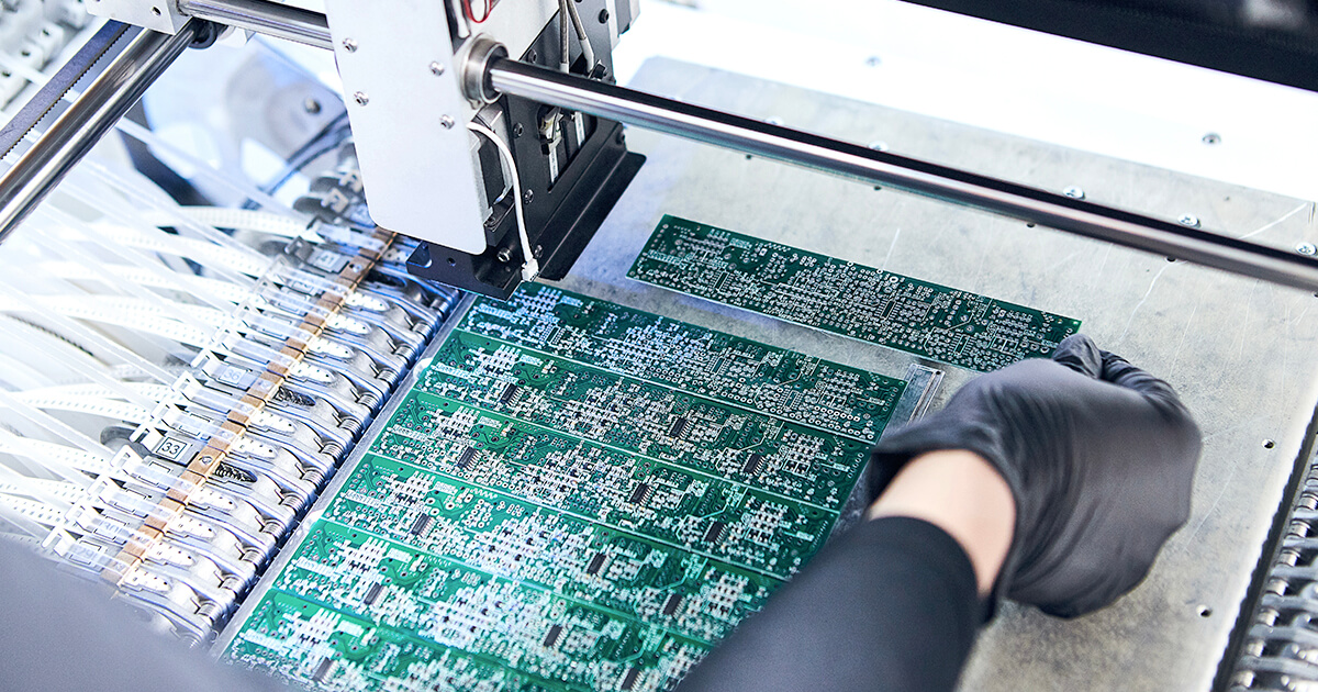 A gloved engineer tests a series of rectangular printed circuit boards in a laboratory environment. | Sourcengine