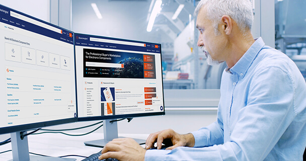 A man seated at a desk in an office environment looks at the Sourcengine homepage on his computer display. 