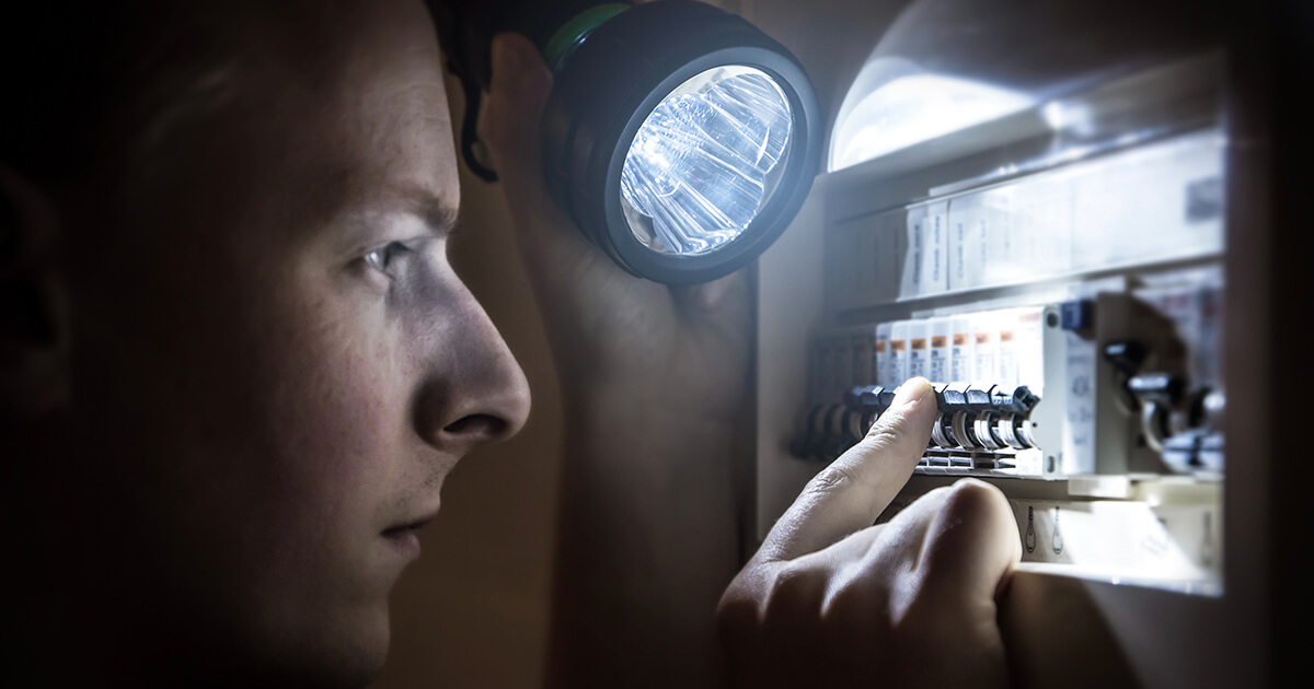 A person shines a flashlight on a circuit breaker in a darkened area. 