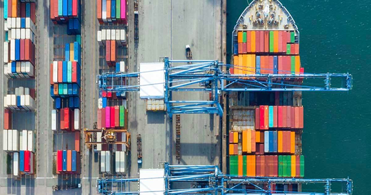 An ariel photo of a port filled with shipping containers and a packed cargo ship. 