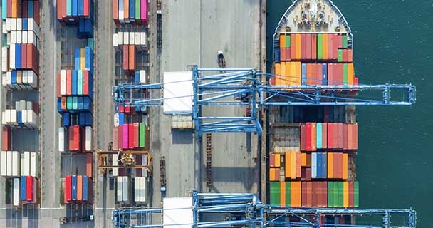 An ariel photo of a port filled with shipping containers and a packed cargo ship. 