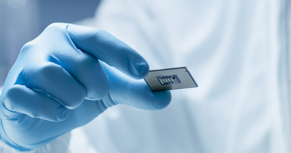 A close-up of an engineer in personal protective gear inspecting a CPU.