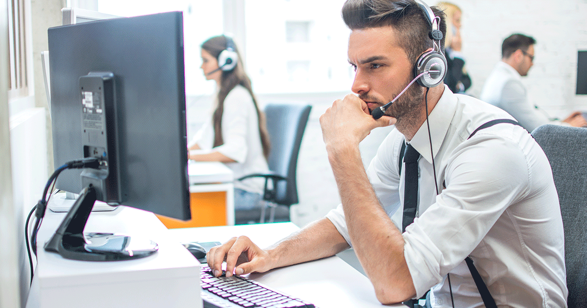 An image of a professional buyer wearing a headset carefully exams their computer screen in an open office space.