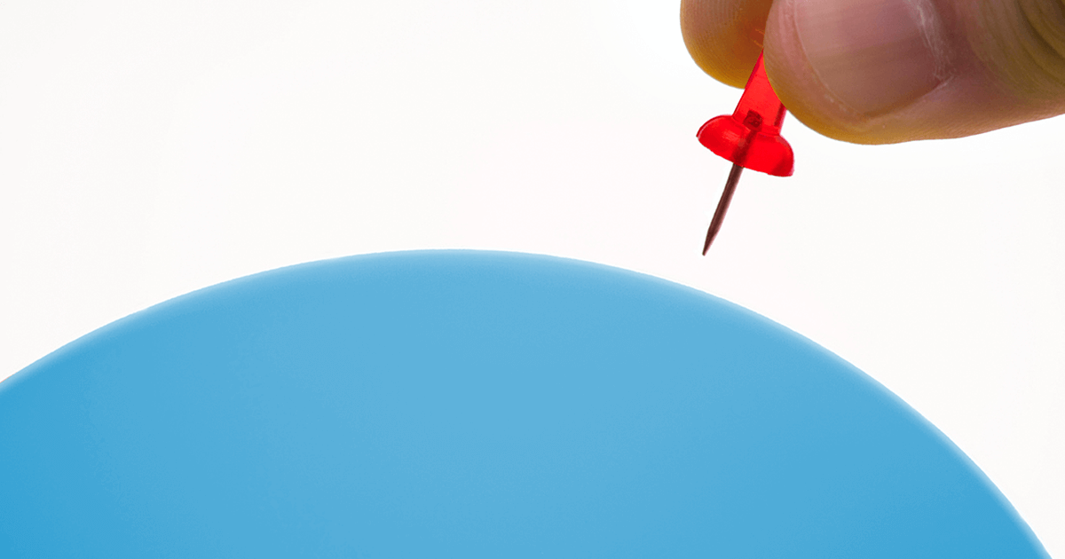Two fingers ominously hold a pushpin over a fully inflated balloon