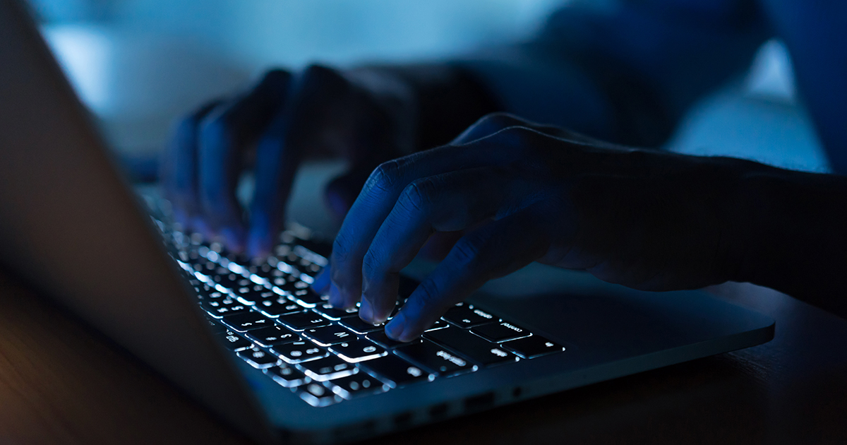 A hacker using a laptop keyobard in the dark